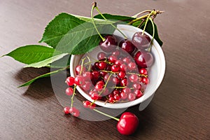 Green cherry leaves, red currant sprigs and ripe cherries in a white bowl closeup