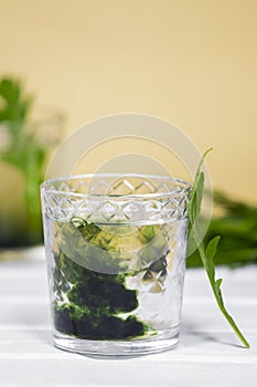 Green Chlorophyll drink in glass with water drops on white table, Orange Background. Antioxidant food and drinks.