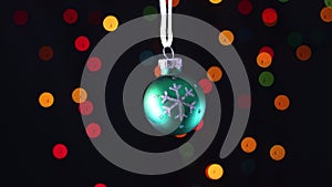 Green Christmas ornament with glitter snowflake swing with blinking lights behind