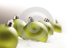 Green Christmas Ornaments on Snow Over a Grey Background