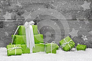 Green Christmas presents with snow on grey wooden background for