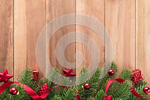 Green Christmas tree leaves with shiny red ornaments on wood background