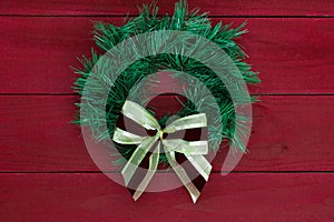 Green Christmas wreath with gold bow hanging on rustic red wooden background