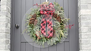 Green christmas wreath from pine or fir and red ribbon on door, New Year decor.