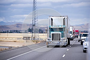 Green classic big rig semi truck reefer unit on traffic road