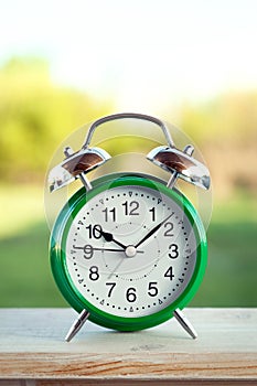 Green clock on old wooden table in the summer garden on a sunny