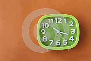 Green clock with white numbers and arrows on orange background