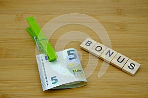 A green clothespin tightens a banknote on a wooden table with written, bonus. Housewives bonus concept
