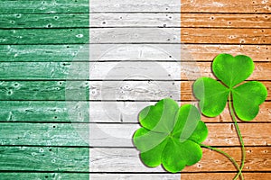 Green clover leaves or shamrocks on wooden background in the color of Irish flag.