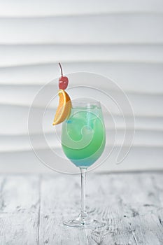 green cocktail in a glass with orange and cherry on a skewer, citrus drink, exotic