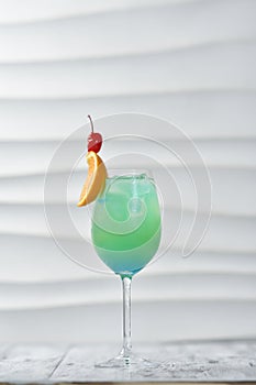 green cocktail in a glass with orange and cherry on a skewer, citrus drink, exotic