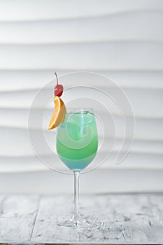 green cocktail in a glass with orange and cherry on a skewer with ice, citrus drink, exotic