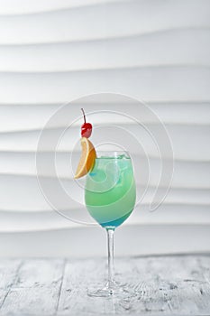 green cocktail in a glass with orange and cherry on a skewer with ice, citrus drink, exotic