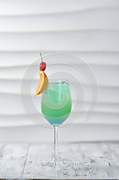 green cocktail in a glass with an orange slice, ice and a cherry on a skewer, an exotic drink