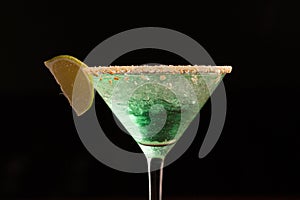 Green cocktail in a martini glass rim covered with salt. with a slice of lime. close-up on a black background
