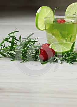Green cocktail on wooden background, decorated with rosemary, strawberry and lime