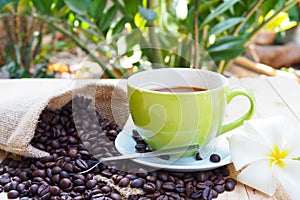 Green coffee cup with burlap sack of coffee beans on wooden table