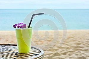 Green color smoothie with purple orchid on the wooden table with the beautiful sea background, copy space