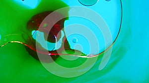 Green colored ink water surface with red oil drop blowing by wind, abstract background. Slow motion.