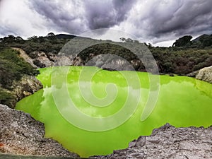 A green-coloured geothermally active lake in the Wai-O-Tapu park in New Zealand under moody clouds