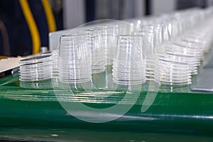 Green conveyor belt with rows of round plastic transparent food containers with lids. Production line for molding