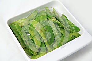 Green cooked stir-fried vegetable snow peas bean on square rectangular plate white background