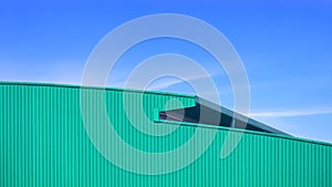 Green Corrugated metal curved Roof of large Warehouse Building in modern style against blue sky Background