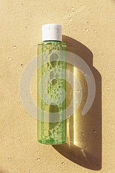 Green cosmetic bottle with lotion or tonik on beige background, strong shadows. Natural organic moisturizing cosmetics