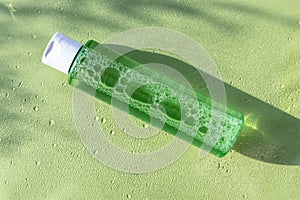 Green cosmetic bottle with tonik, strong shadows. Natural organic moisturizing cosmetics. Top view, flat lay