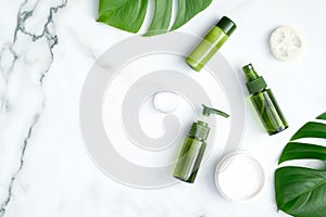 Green cosmetic bottles with monstera tropical leaf on marble background. SPA natural organic beauty products for skincare, body