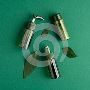 Green cosmetic bottles with plant leaves on green background. Natural organic beauty products, skin care concept