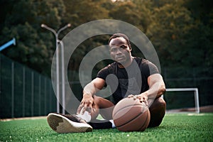 On the green court. Young black man is with basketball ball outdoors