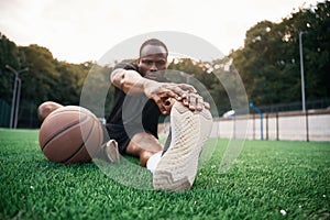 On the green court. Young black man is with basketball ball outdoors