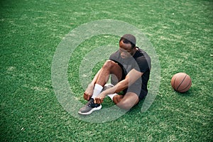 On the green court. Young black man is with basketball ball outdoors