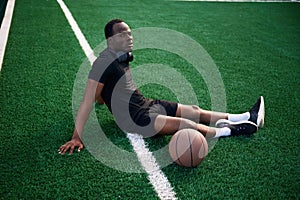 On the green court. Young black man is with basketball ball outdoors