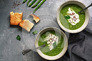 Green cream asparagus soup with crispy toasts on a gray background. Overhead view, copy space