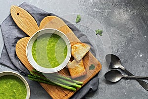 Green cream asparagus soup on a cutting board with toast, gray background. Top view, copy space, flat lay