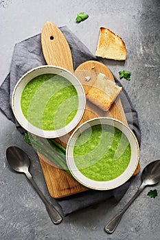 Green cream asparagus soup with toast on a cutting board, gray concrete background. Vegan Vegetarian Soup. Top view, flat lay