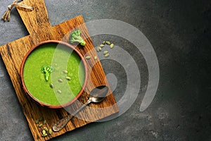 Green cream broccoli soup with pumpkin seeds in a ceramic bowl on a cutting board, dark rustic background. Top view. Vegetarian