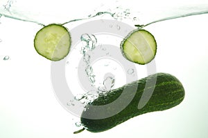 Green Cucumber and two slices in water splash on white background