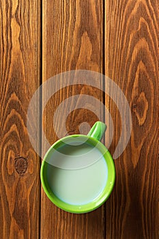 Green cup of milk on a vintage wooden background. Flat top view. Green mug with milk