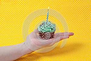 Green cupcake and a birthday candle on hand