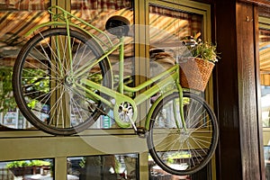 Green decorative bicycle hanging on a glass window in the street