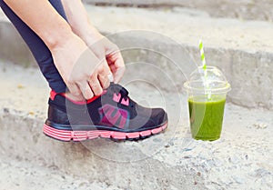 Green detox smoothie cup and woman lacing running shoes before w