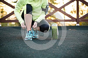 Green detox smoothie cup and woman lacing running shoes before w