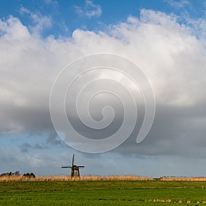 Green dike with windmill, blue winter sky and coulds