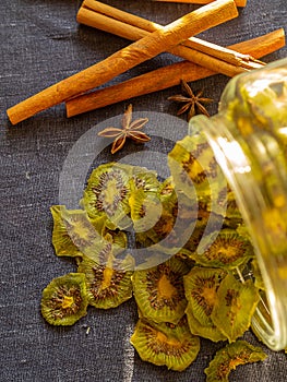 Green dried kiwi fruits lie scattering in a glass jar and cinnamons on the background