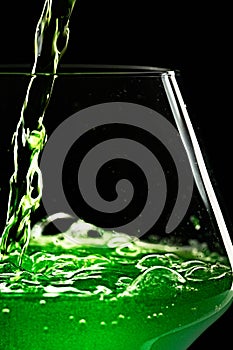 Green drink is poured into a glass. Black background