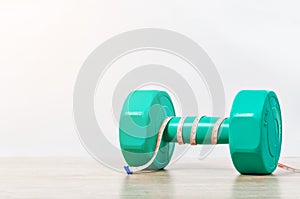 Green dumbbell and measuring tape on wooden background.