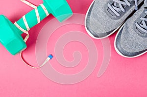 Green dumbbell and sneakers on pink background.